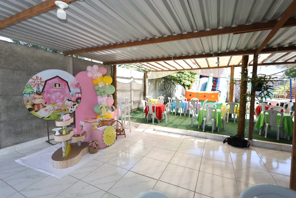 Salão do espaço com painel de festa e mesas postas no quintal ao fundo